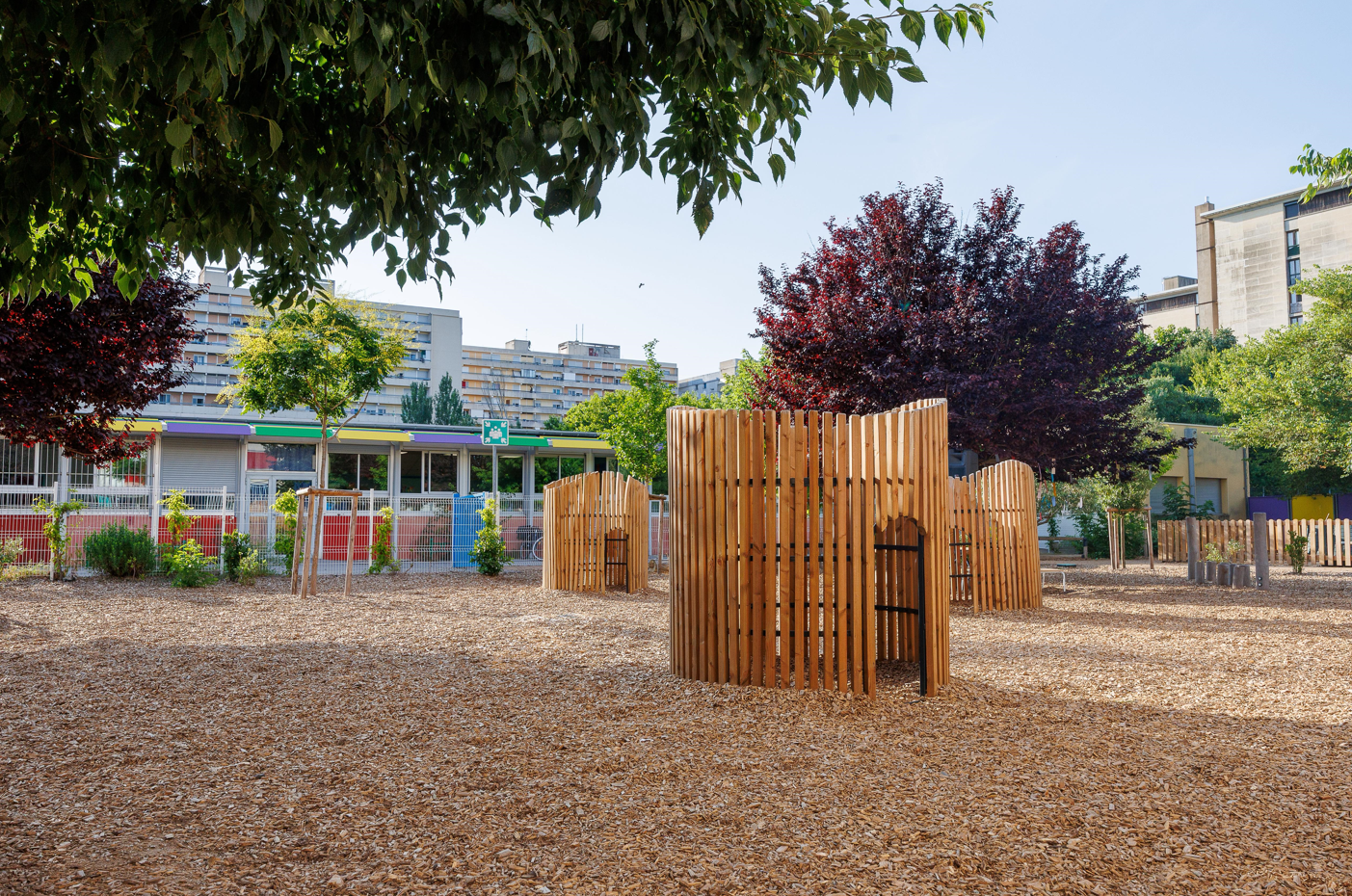 cour végétalisée cabanes en bois arbre copeaux au sol jeux 
