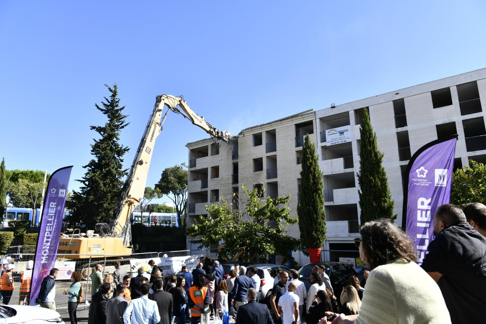 personnes regardant la pelle mecanique à grand bras débutant la démolition d'un bâtiment de la résidence Neptune à la Mosson