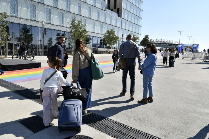 voyageurs avec valises rainbow flag parvis de la gare batiment