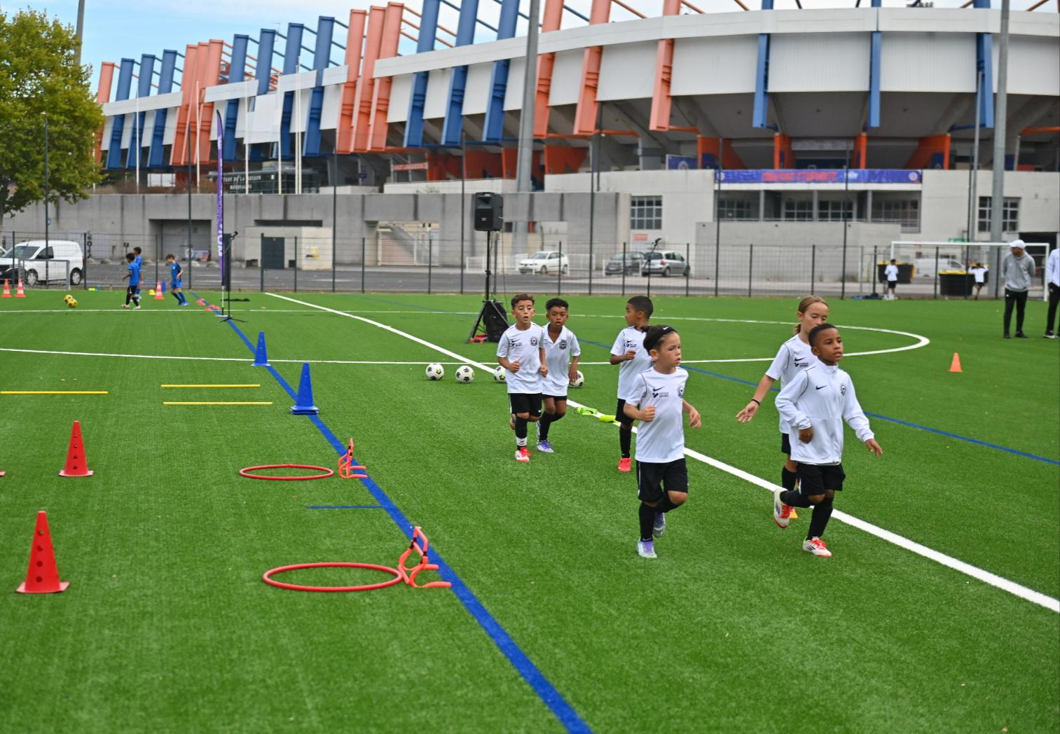 plots et cerceaux, enfants en tenue qui courent, pelouse synthétique neuve, stade la Mosson en arrière-plan