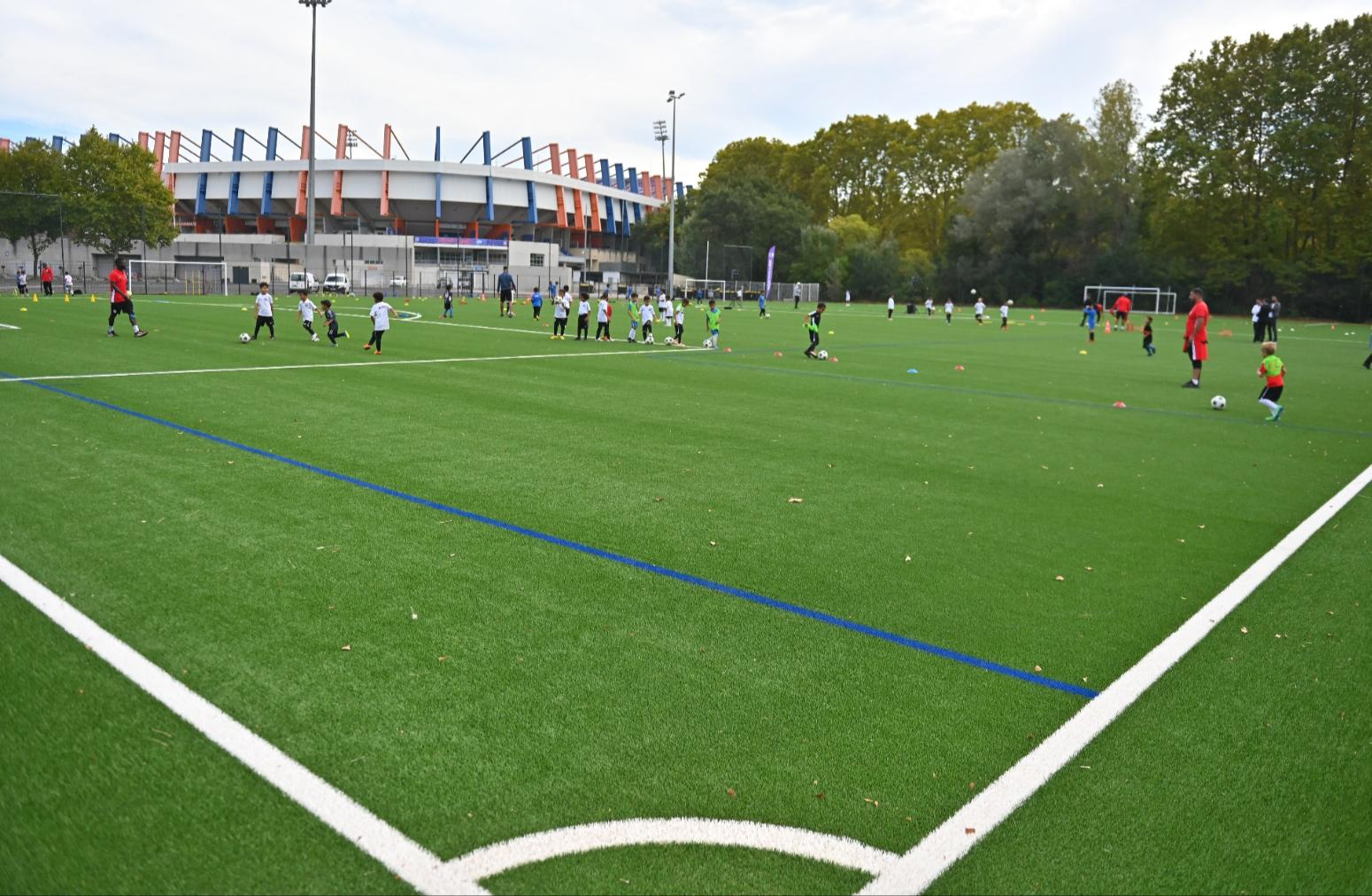 nouvelle pelouse synthétique du stade annexe, stade de la Mosson en arrière-plan, enfants jouant au football, arbres
