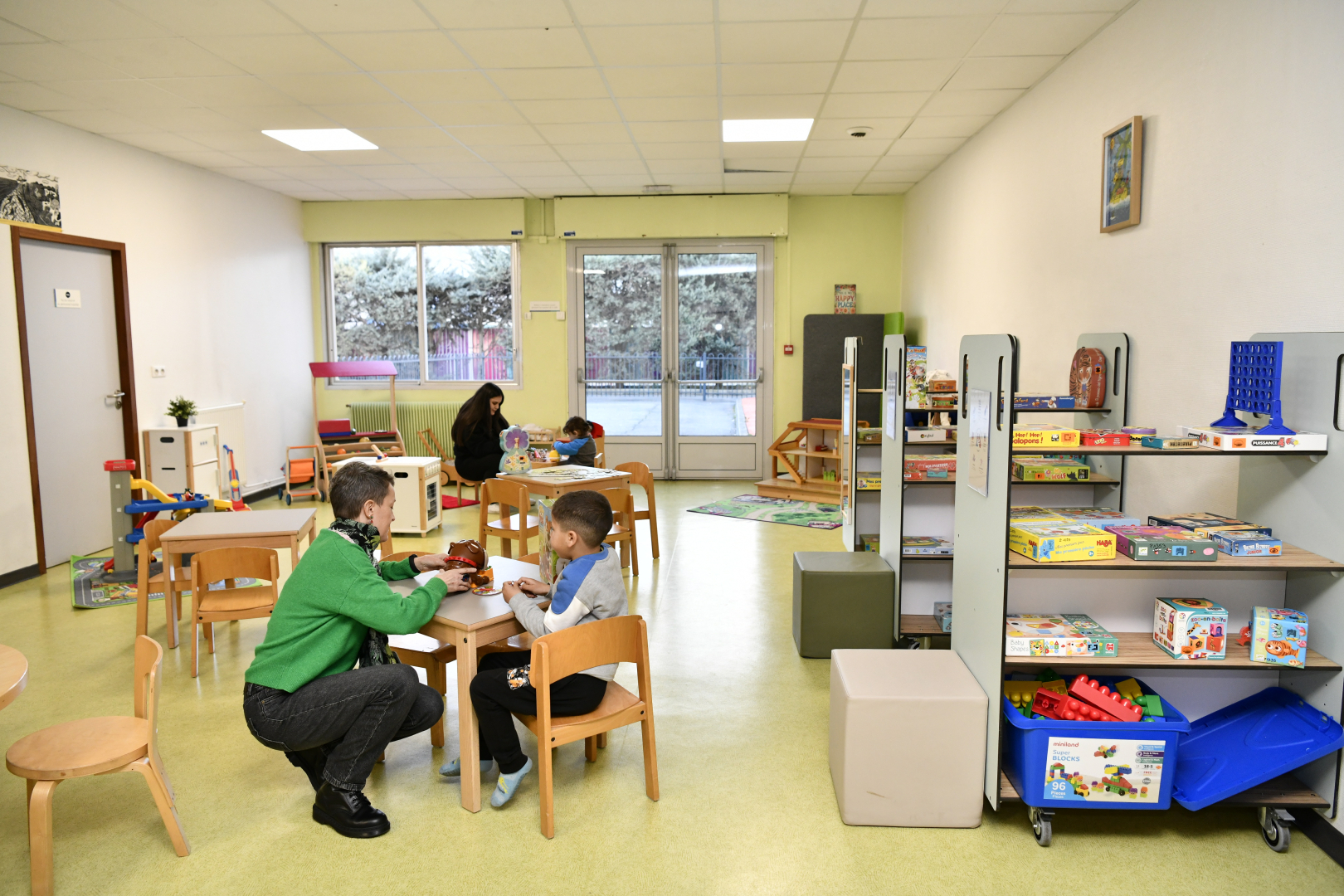 ludothèque tables et chaises à hauteur d'enfant jeux étagères adultes enfants qui jouent fenêtre