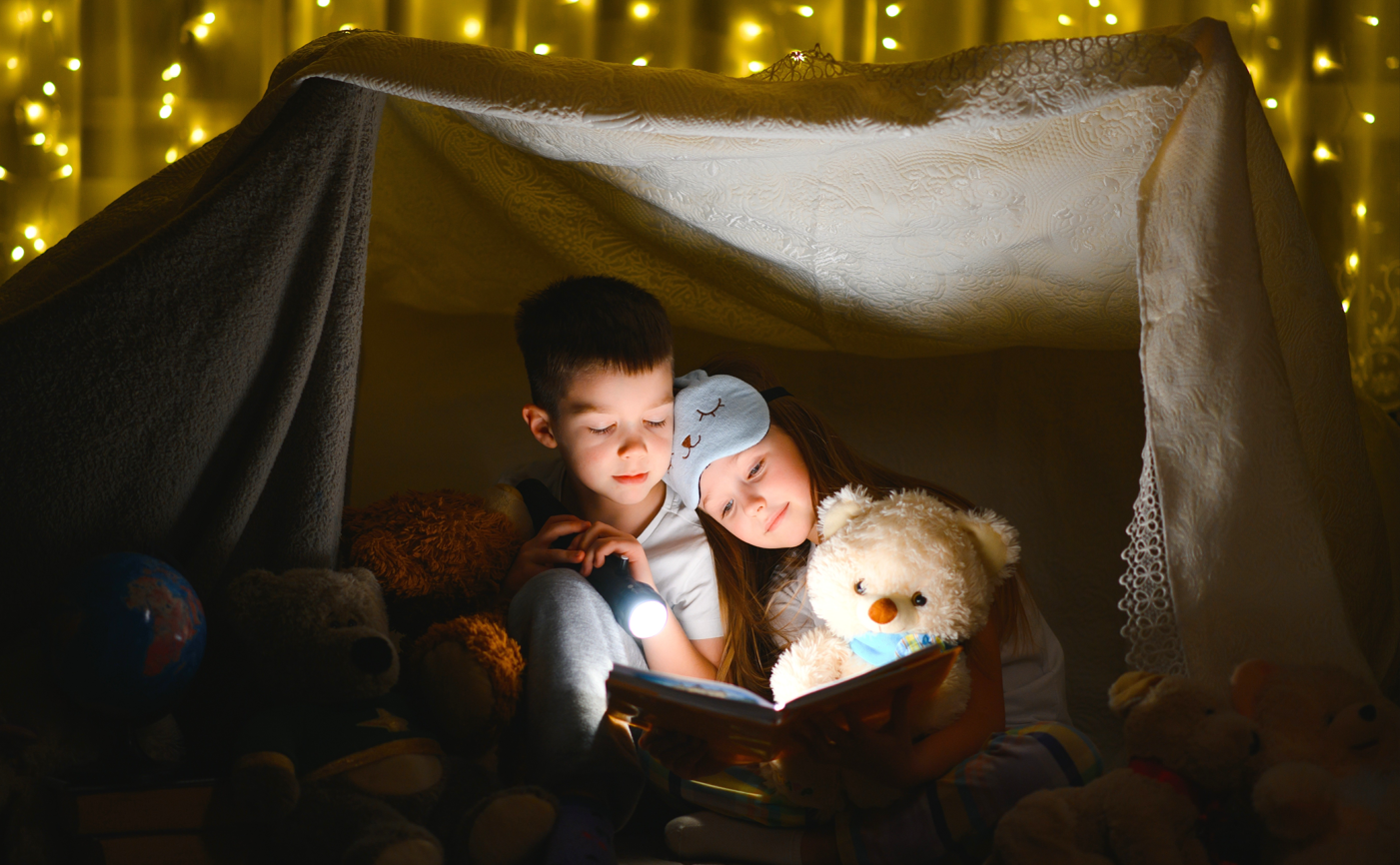 Enfant et nounours lisant sous une tente éclairée par des ampoules