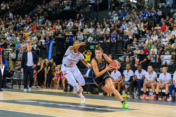 Julie Pospisilova en action contre Villeneuve d’Ascq à la Sud de France Arena, parquet, banc, coach et public en arrière-plan