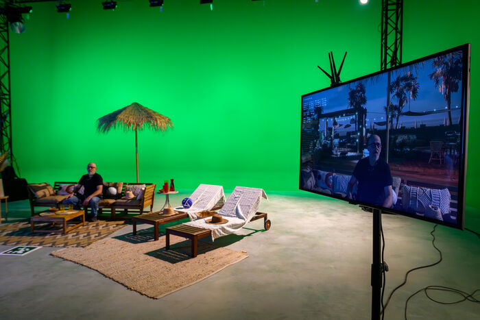 Plateau de tournage, fond vert, figurant, transat, parasol, accessoires, écran visualisant les effets spéciaux de l'arrière plan