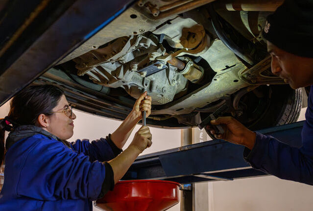 Sarah travaille sur une voiture, outil, coll&egrave;gue qui &eacute;claire le dessous du v&eacute;hicule