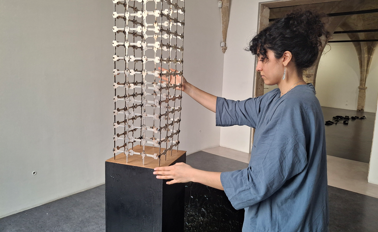 Melika Sadeghzadeh, en chemise bleue, installe une structure metallique sur une sculpture en bois