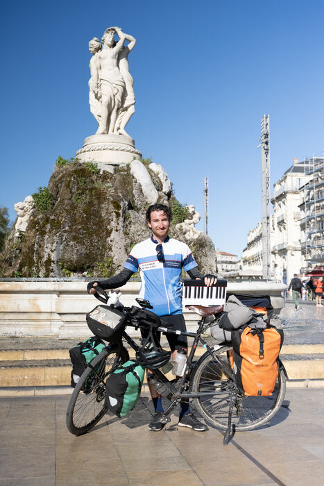 Djivann, son vélo et une partie de son piano démontable devant la statue des Trois Grâces, point d'arrivée de son tour du monde