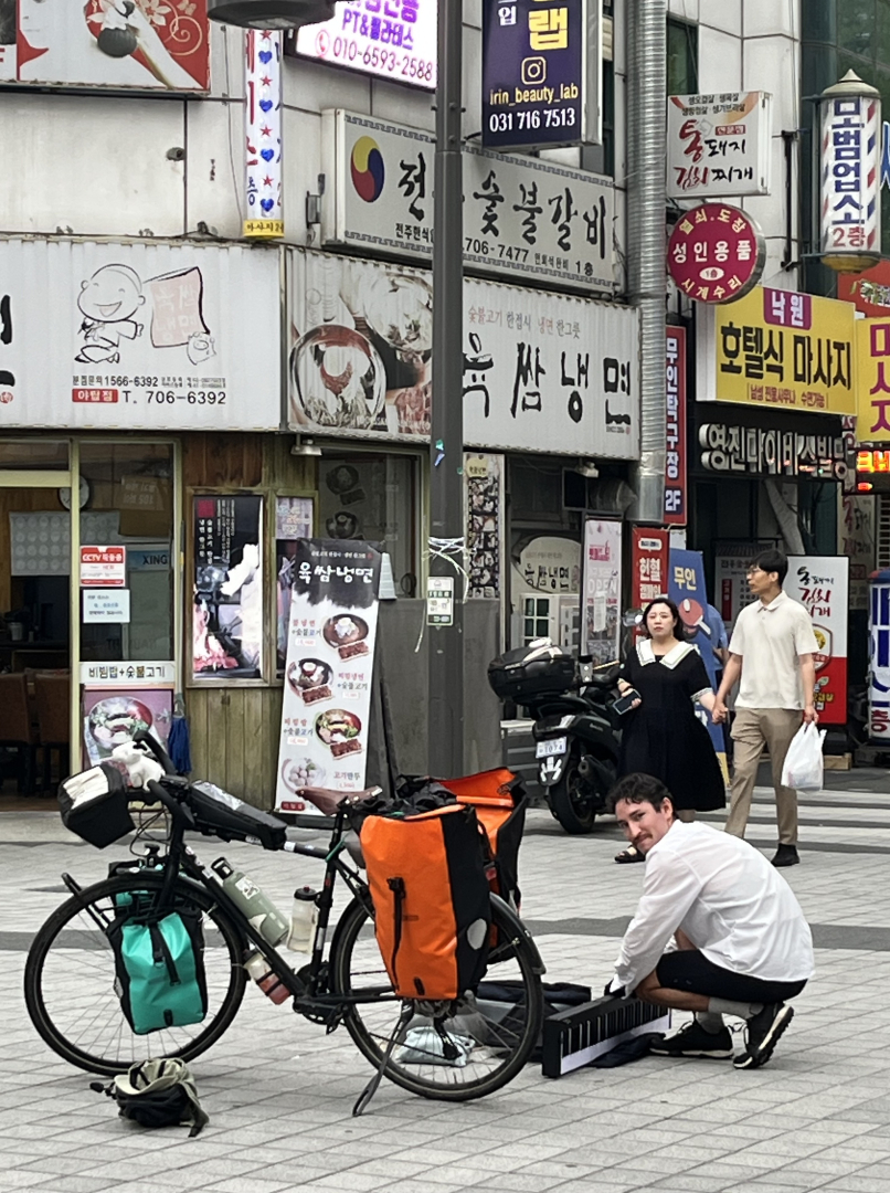 rue en Corée avec boutiques et publicités, vélo, Djivann en train d'installer son piano, passants