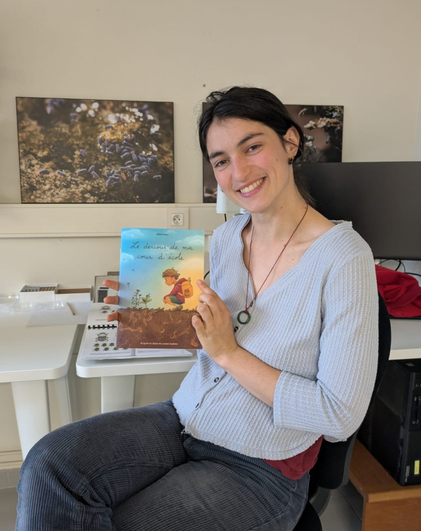 La post-doctorante Louise Eydoux pose avec la BD illustrant sa th&egrave;se, photos et ordinateur en arri&egrave;re-plan