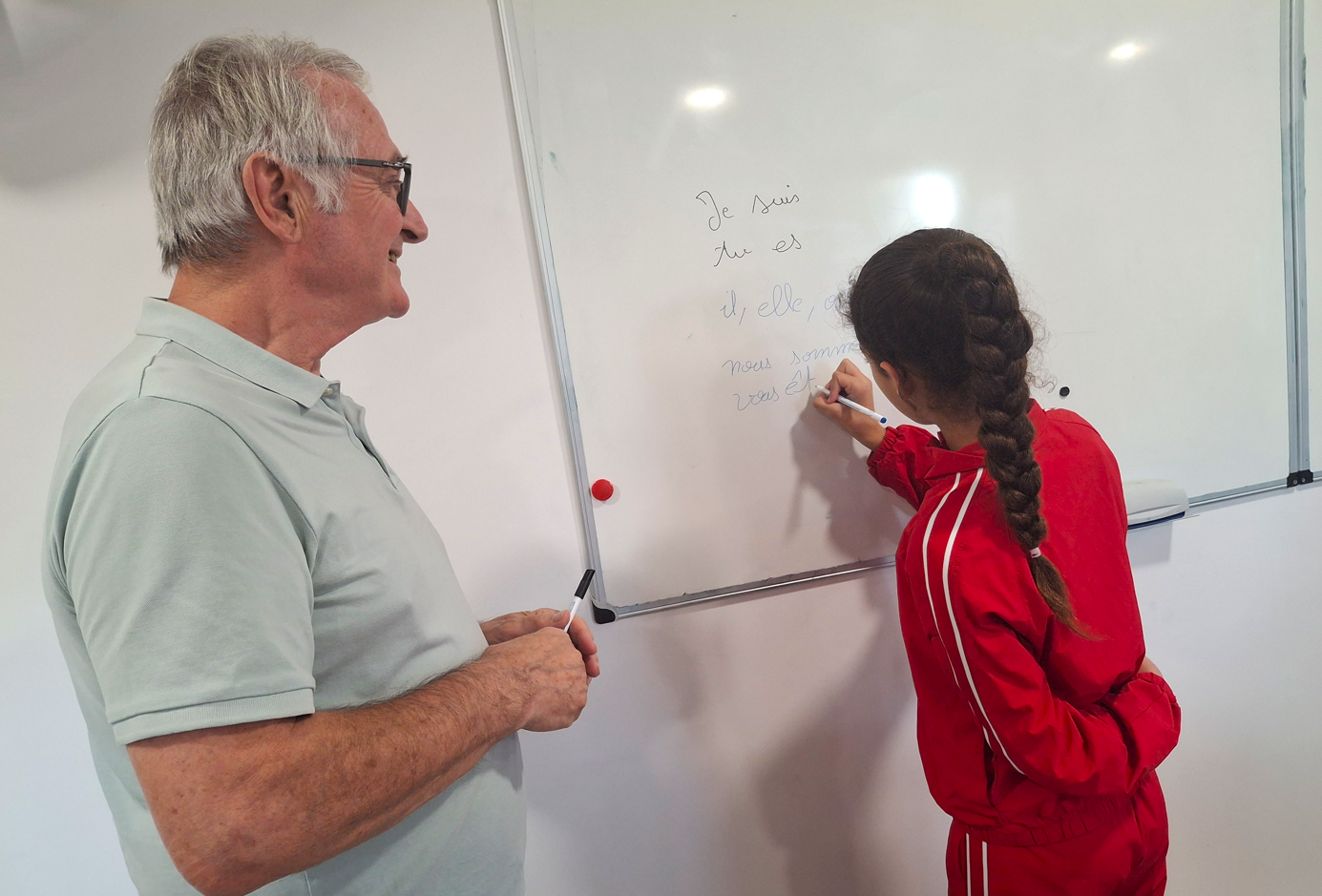 Photo de Francis, bénévole et une petite fille qui écrit au tableau