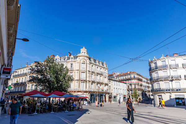 place Saint Denis aujourd'hui avec ciel bleu, terrasses, piétons, arbre, façades nettoyées, rails du tram