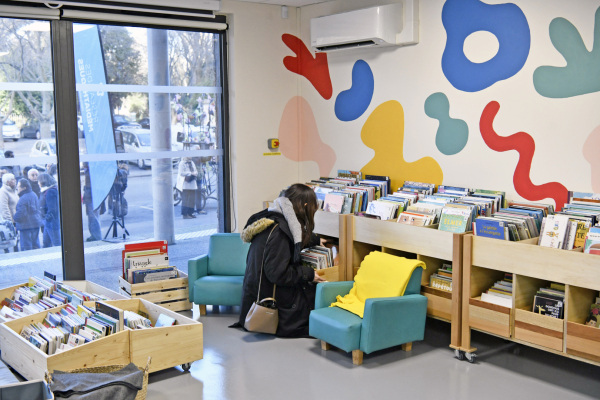 espace chaleureux avec petits sièges et coussins, personne cherchant dans les bacs à livres pour enfants, murs décorés de couleurs vives