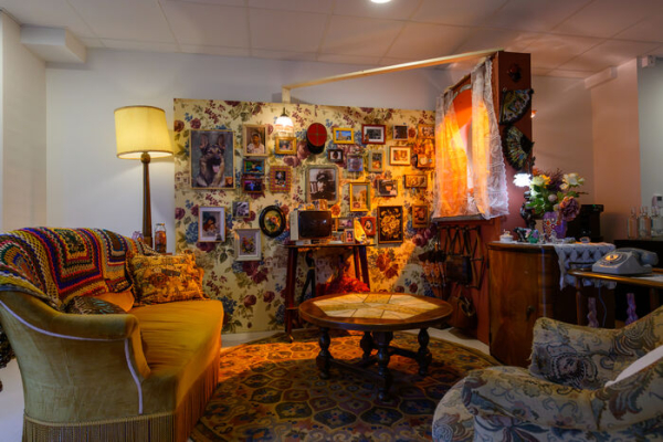 décor de tournage avec fauteuils, lampe, table, tapisseries, photos encadrées au mur, autres accessoires