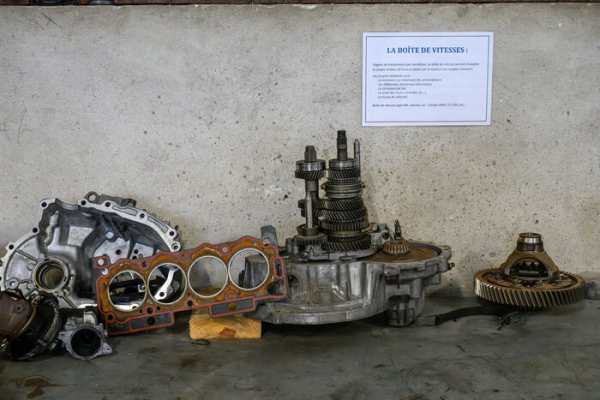 &eacute;l&eacute;ments de moteur et boite de vitesse de voiture au sol, pancarte explicative au mur