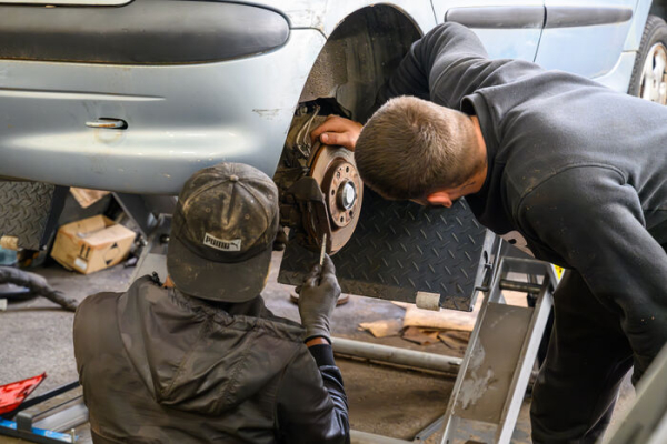 deux "apprentis" m&eacute;caniciens travaillent sur une voiture au niveau des roues arri&egrave;res