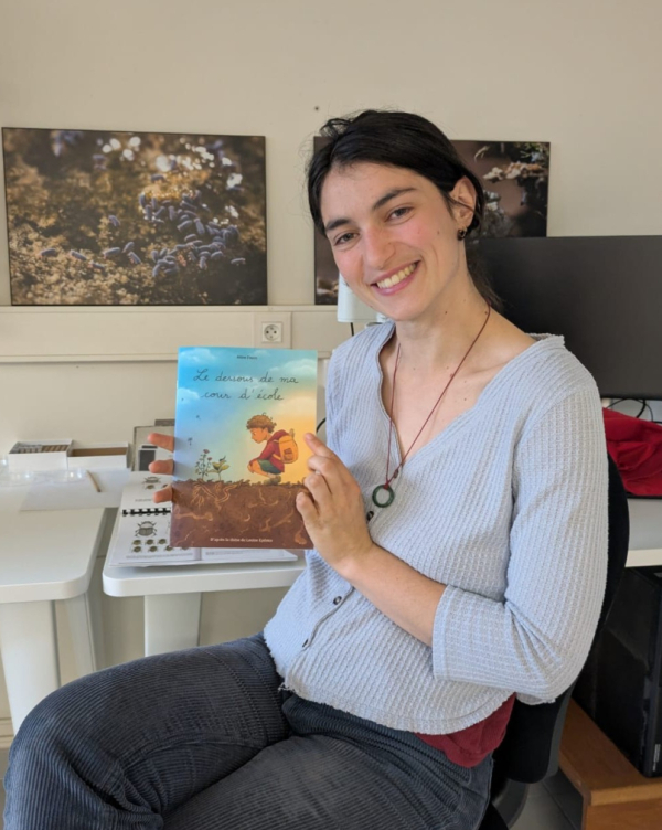 La post-doctorante Louise Eydoux pose avec la BD illustrant sa th&egrave;se, photos et ordinateur en arri&egrave;re-plan