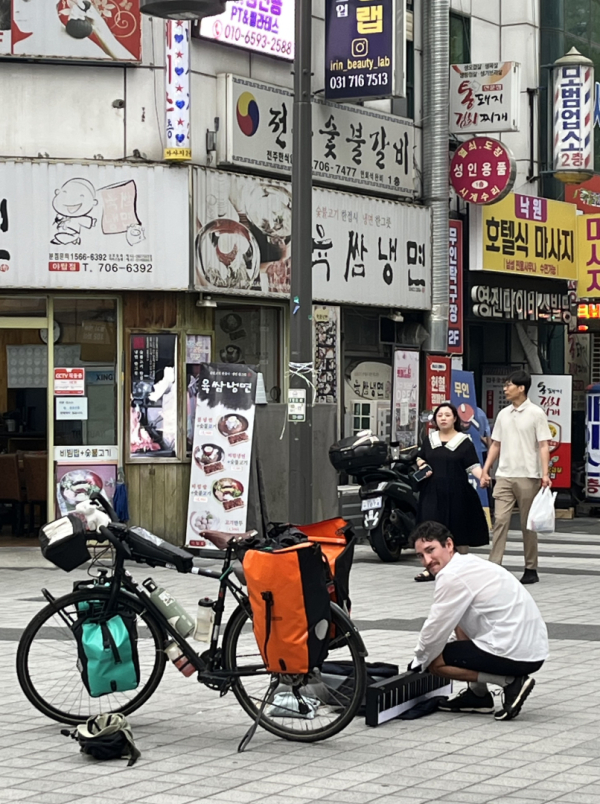 rue en Corée avec boutiques et publicités, vélo, Djivann en train d'installer son piano, passants