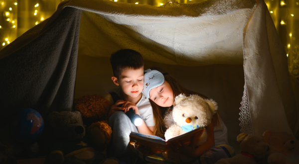 Enfant et nounours lisant sous une tente éclairée par des ampoules