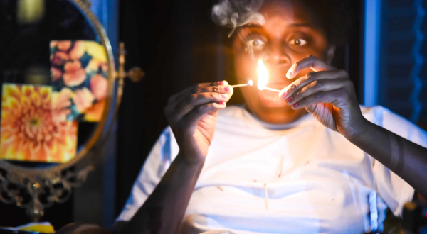 Une femme regarde deux allumettes en train de brûler entre ses doigts