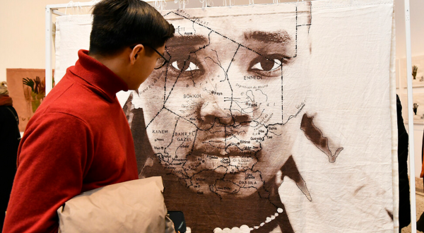 Un visiteur devant l'un des grands paravents mêlant photo et broderie et représentant un visage de femme