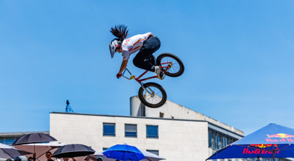 Bikeuse dans les airs avec son vélo, ciel, tribune, parasols publicitaires, batîment