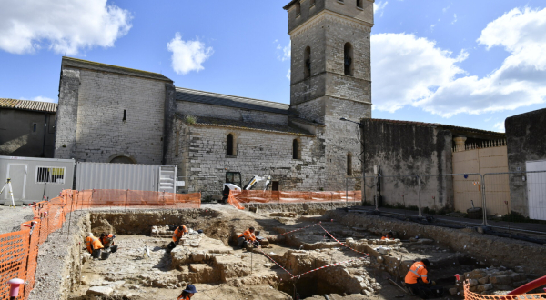 site de fouilles, archéologues, clôture de protection, église du XIe siècle en arrière-plan, ciel
