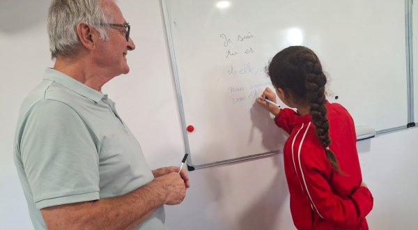 Photo de Francis, bénévole et une petite fille qui écrit au tableau
